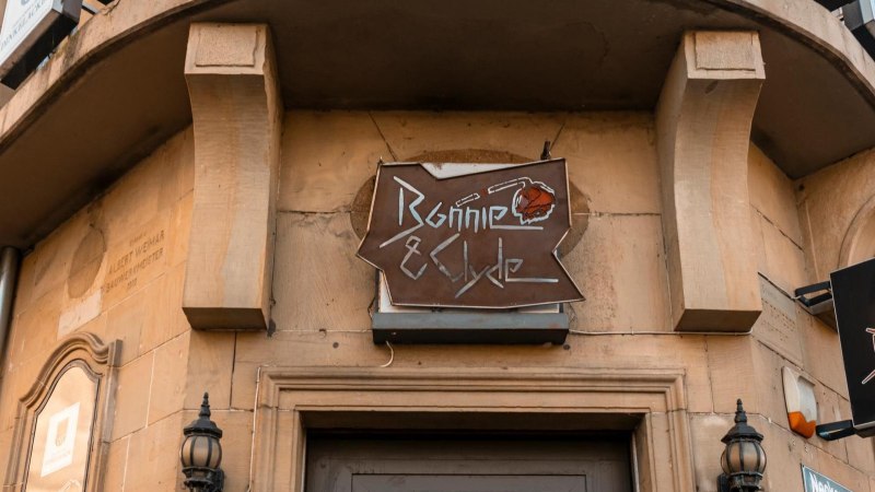 Ein Schild mit der Aufschrift 'Bonnie & Clyde' hängt an einem Gebäude. Die Fassade ist aus Stein, und es gibt dekorative Laternen., © SMG. Sarah Schmid Ein Schild mit der Aufschrift 'Bonnie & Clyde' hängt an einem Gebäude. Die Fassade ist aus Stein, und es gibt dekorative Laternen., © SMG. Sarah Schmid