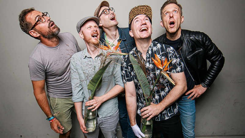 F&uuml;nf M&auml;nner blicken &uuml;berrascht nach oben. Zwei von ihnen halten Blumenstr&auml;u&szlig;e. Sie tragen l&auml;ssige Kleidung und wirken fr&ouml;hlich., &copy; Peerplex