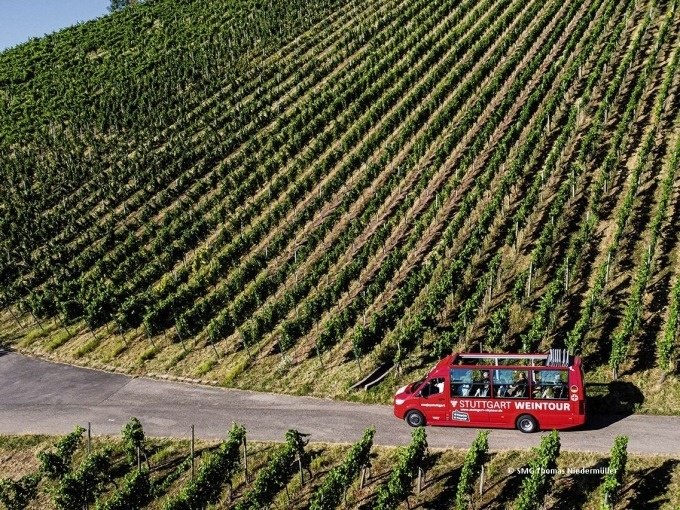 Ein roter Tourbus mit der Aufschrift 'Stuttgart Weintour' fährt an einem Weinberg entlang., © SMG, Thomas Niedermüller Ein roter Tourbus mit der Aufschrift 'Stuttgart Weintour' fährt an einem Weinberg entlang., © SMG, Thomas Niedermüller