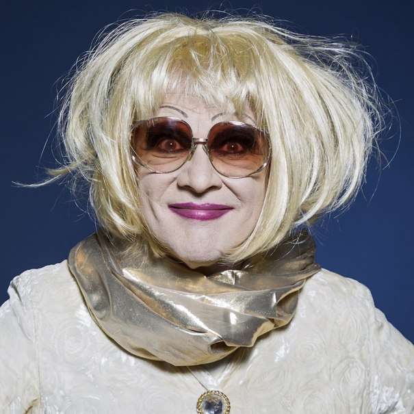 Person with blond wig, sunglasses and golden scarf in front of a blue background., &copy; Renitenztheater Stuttgart e.V.