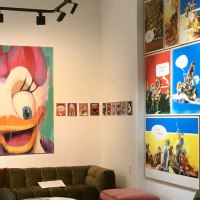 A gallery displays colorful Pop Art paintings of comic book characters and modern artworks. A large painting of a duck dominates the wall. There is a sofa in the room., © Galerie Z A gallery displays colorful Pop Art paintings of comic book characters and modern artworks. A large painting of a duck dominates the wall. There is a sofa in the room., © Galerie Z