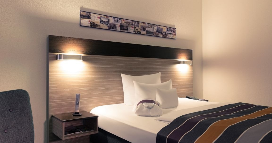 A modern hotel room with a double bed, a striped comforter, two wall sconces, and a decorative painting above the bed., &copy; Mercure Hotel Stuttgart Gerlingen