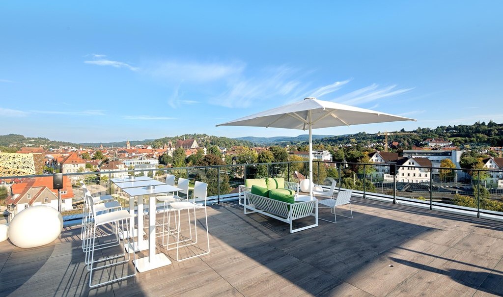 Modern roof terrace with white furniture, parasol and view of a cityscape with hills in the background., © Hotel am Remspark Modern roof terrace with white furniture, parasol and view of a cityscape with hills in the background., © Hotel am Remspark