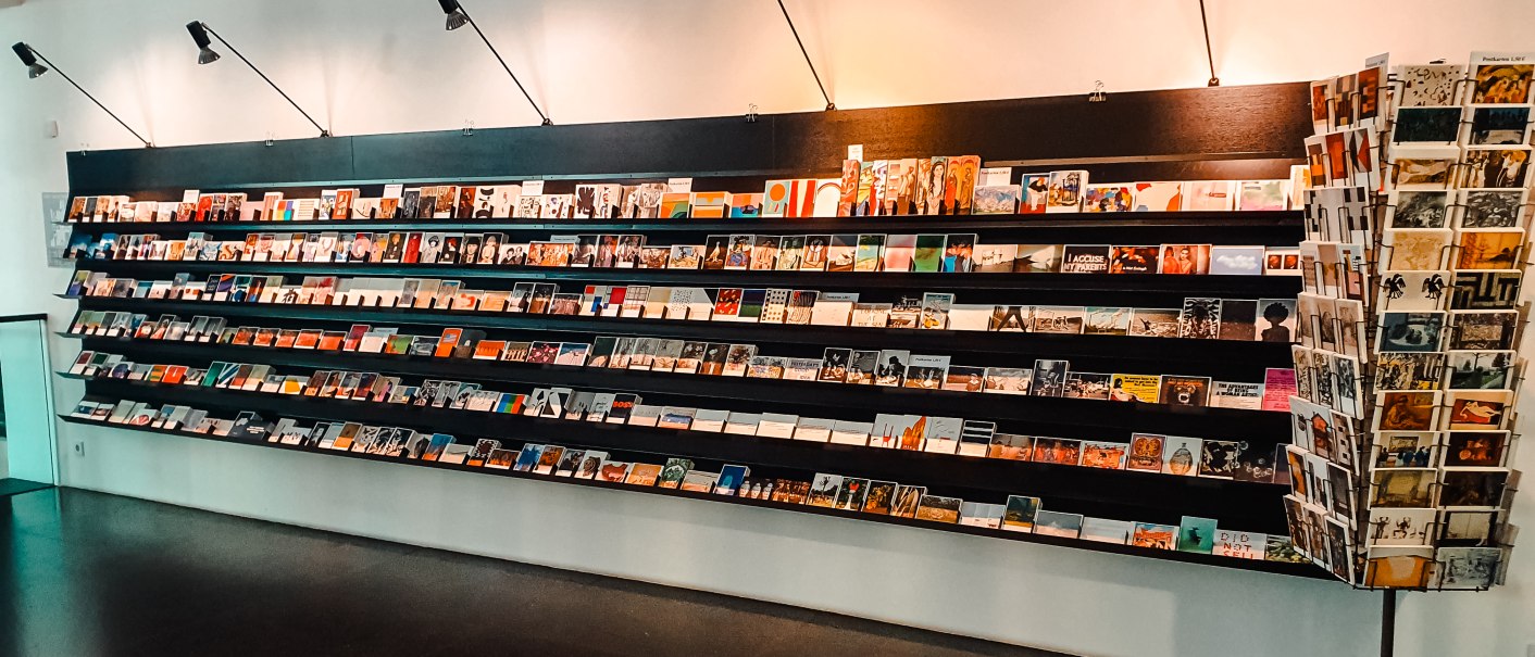 Ein langes Regal mit zahlreichen Postkarten im Kunstmuseum. Die Karten sind in mehreren Reihen angeordnet und von Lampen beleuchtet., © Walther König Ein langes Regal mit zahlreichen Postkarten im Kunstmuseum. Die Karten sind in mehreren Reihen angeordnet und von Lampen beleuchtet., © Walther König