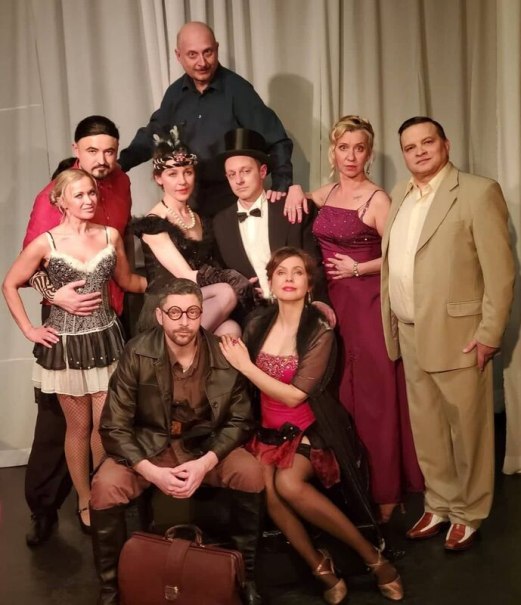 Nine people in different costumes pose on a stage. They wear elegant and themed clothing, appropriate for a theater performance., © Theater Atelier Nine people in different costumes pose on a stage. They wear elegant and themed clothing, appropriate for a theater performance., © Theater Atelier