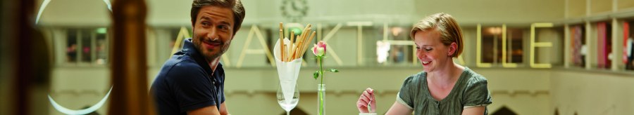 Ein Paar sitzt l&auml;chelnd an einem Tisch in einem Caf&eacute;. Im Hintergrund sind gro&szlig;e Buchstaben an der Wand sichtbar., &copy; TMBW, Christoph D&uuml;pper