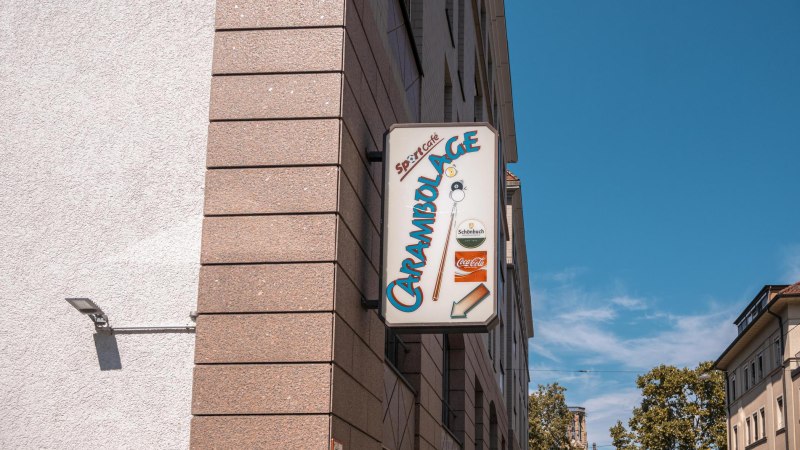 Ein Schild mit der Aufschrift 'Carambolage' h&auml;ngt an einer Geb&auml;udewand. Der Himmel ist klar und blau., &copy; SMG, Sarah Schmid