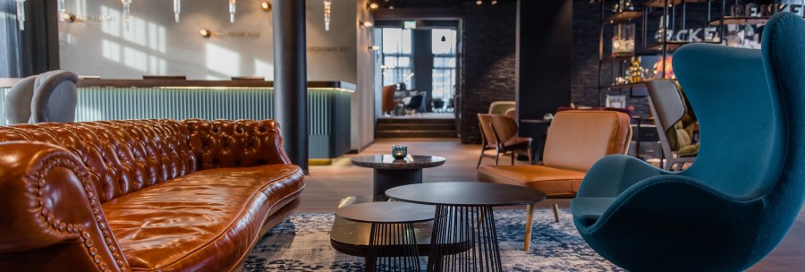 Moderne Hotellobby mit braunem Ledersofa, blauem Sessel, Couchtischen und stilvoller Beleuchtung. Elegantes, gemütliches Ambiente., © TOMAS Moderne Hotellobby mit braunem Ledersofa, blauem Sessel, Couchtischen und stilvoller Beleuchtung. Elegantes, gemütliches Ambiente., © TOMAS
