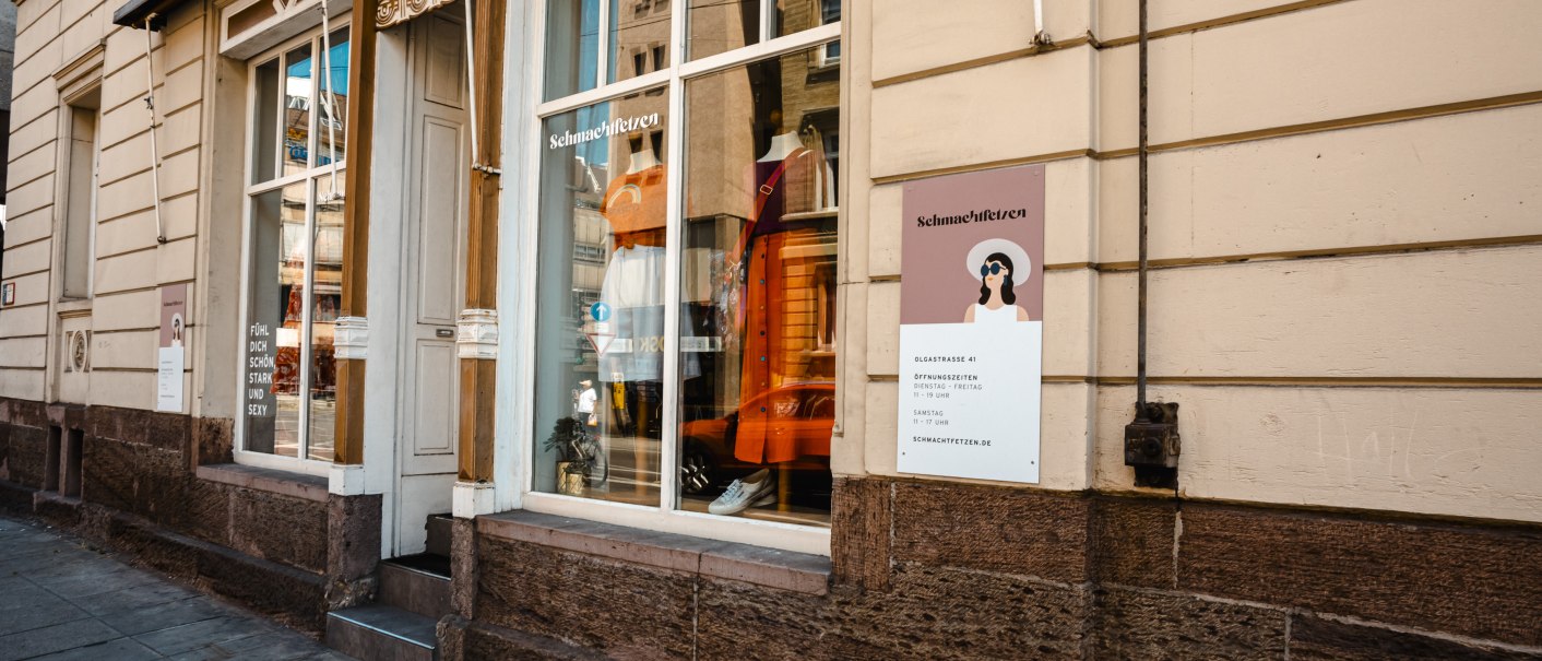 Ein Laden namens Schmachtfetzen mit Schaufenster und Schild an einer beigen Hauswand. Im Fenster sind Kleidungsstücke ausgestellt., © SMG Stuttgart Marketing GmbH - Sarah Schmid Ein Laden namens Schmachtfetzen mit Schaufenster und Schild an einer beigen Hauswand. Im Fenster sind Kleidungsstücke ausgestellt., © SMG Stuttgart Marketing GmbH - Sarah Schmid