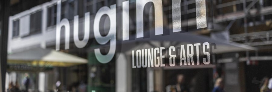 Reflection of the lettering 'huginn LOUNGE & ARTS' on a glass surface, blurred street scene in the background., &copy; SMG, Sarah Schmid