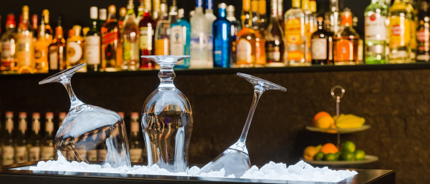 Three upturned glasses on ice in front of a bar. Numerous colorful bottles can be seen in the background. On the right is an etagere with fruit., &copy; MASEVEN Stuttgart SI-Centrum