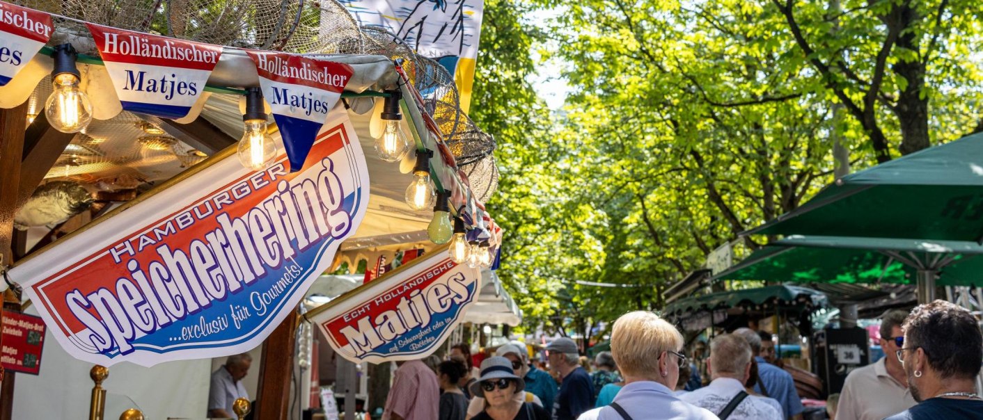 Menschen schlendern über den Hamburger Fischmarkt auf dem Karlsplatz, umgeben von Ständen mit Matjes und Fischspezialitäten unter grünen Bäumen., © Stuttgart-Marketing GmbH, Sarah Schmid Menschen schlendern über den Hamburger Fischmarkt auf dem Karlsplatz, umgeben von Ständen mit Matjes und Fischspezialitäten unter grünen Bäumen., © Stuttgart-Marketing GmbH, Sarah Schmid
