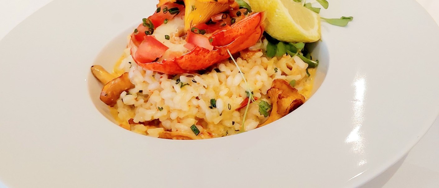 Risotto mit Hummer, Pilzen und Zitronenscheibe auf weißem Teller serviert., © Erikson Hotel Risotto mit Hummer, Pilzen und Zitronenscheibe auf weißem Teller serviert., © Erikson Hotel