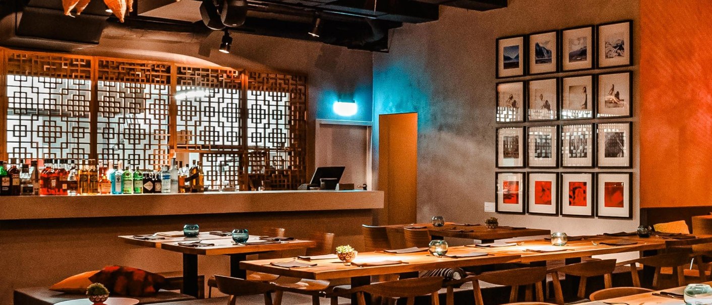 Stilvolles Restaurant mit Holztischen, dekorativen Gittern und einer Bar. An der Wand hängen gerahmte Bilder, die Atmosphäre ist warm und einladend., © Breitengrad17 Stuttgart