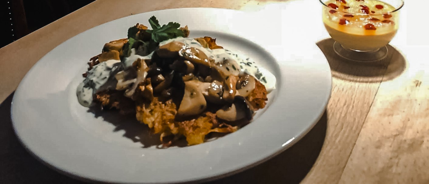 Ein Teller mit einem Gericht und ein Dessert auf einem Tisch, daneben ein Eimer mit Tulpen. Im Hintergrund ein Gem&auml;lde einer Frau., &copy; Weinstube Fr&ouml;hlich Verwaltungs GmbH