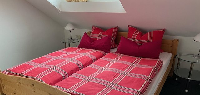 Gemütliches Schlafzimmer mit einem Holzbett, roten karierten Bettbezügen und zwei Nachttischen unter einem Dachfenster., © Weinhof am Württemberg Gemütliches Schlafzimmer mit einem Holzbett, roten karierten Bettbezügen und zwei Nachttischen unter einem Dachfenster., © Weinhof am Württemberg