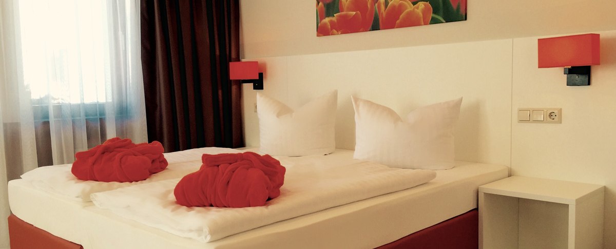 Ein gem&uuml;tliches Hotelzimmer mit Doppelbett, roten Badem&auml;nteln und einem Tulpenbild an der Wand. Die Beleuchtung ist warm und einladend., &copy; TOMAS