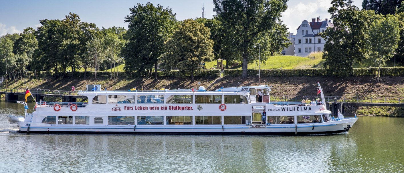 The passenger ship MS Wilhelma sails on a river, surrounded by trees and a building in the background. Inscription: "A Stuttgart resident for life.", © all copyrights are reserved by maks richter