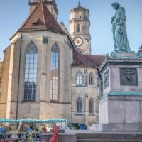 Der Schillerplatz in Stuttgart zeigt eine Statue, historische Gebäude und Marktstände. Im Hintergrund ist eine Kirche mit Turm zu sehen., © SMG Martina Denker