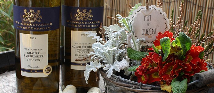 Two bottles of wine, asparagus and strawberries on a wooden table. A flower basket with an 'Art of Queen!' sign stands next to it., © Besenwirtschaft Rauscher Two bottles of wine, asparagus and strawberries on a wooden table. A flower basket with an 'Art of Queen!' sign stands next to it., © Besenwirtschaft Rauscher