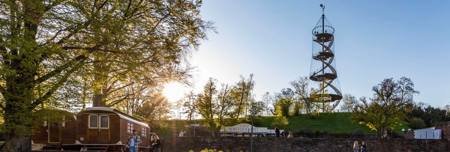 The Killesberg Tower stands in a park surrounded by trees. People are walking at sunset. A waffle stand is visible., © © Stuttgart-Marketing GmbH, Werner Dieterich