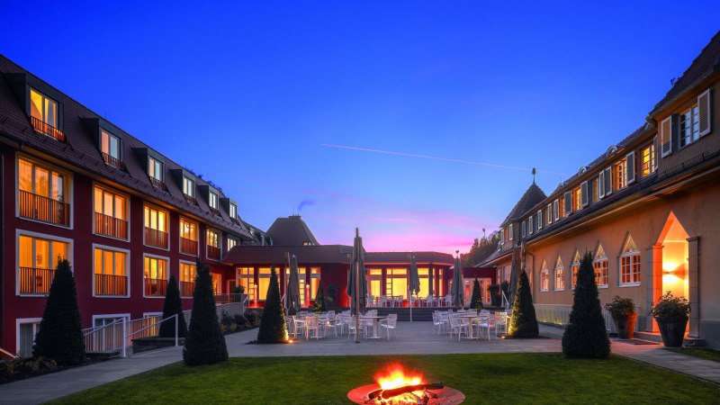 Das Waldhotel Stuttgart bei Dämmerung, mit beleuchteten Fenstern und einer Feuerstelle im Garten. Der Himmel ist blau mit einem rosa Streifen., © Waldhotel Stuttgart GmbH Das Waldhotel Stuttgart bei Dämmerung, mit beleuchteten Fenstern und einer Feuerstelle im Garten. Der Himmel ist blau mit einem rosa Streifen., © Waldhotel Stuttgart GmbH