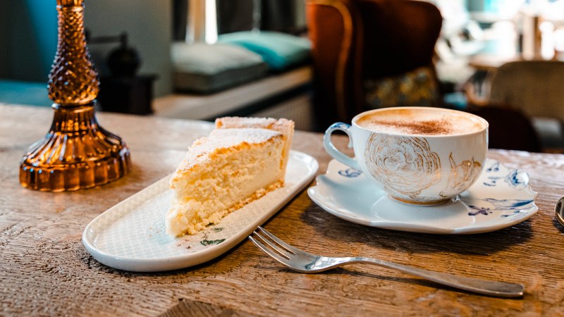 A piece of cake and a cup of coffee on a wooden table in a cozy café. Blurred furniture in the background., © SMG Stuttgart Marketing GmbH - Sarah Schmid