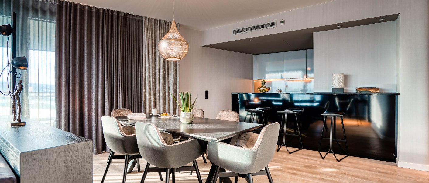 Elegante Suite mit modernem Esstisch, gepolsterten Stühlen und offener Küche. Große Fenster mit Vorhängen und stilvolle Beleuchtung., © CLOUD N°7 APARTMENTS GmbH Elegante Suite mit modernem Esstisch, gepolsterten Stühlen und offener Küche. Große Fenster mit Vorhängen und stilvolle Beleuchtung., © CLOUD N°7 APARTMENTS GmbH