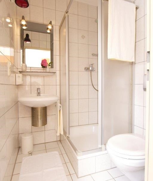Kompaktes Badezimmer mit Dusche, Waschbecken und Toilette. Weiße Fliesen, Handtuchhalter und Spiegel mit Beleuchtung., © Hotel Reinhardtshof Garni