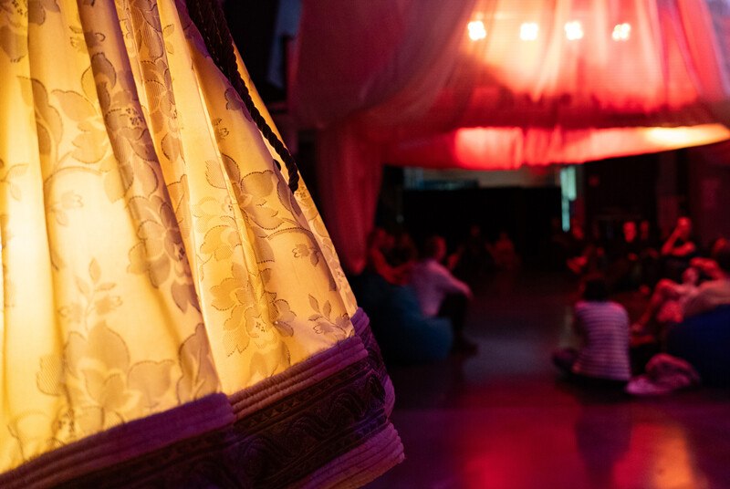 A room with subdued lighting, decorated with fabrics. People sit relaxed on beanbags. An illuminated curtain in the foreground., &copy; W&uuml;rttembergische Staatstheater Stuttgart