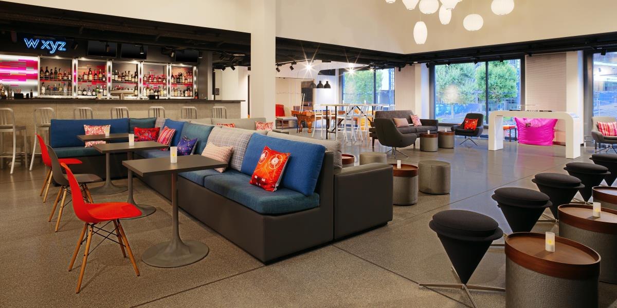 Moderne Lounge mit Bar, bunten Sofas und Tischen, dekoriert mit Kissen. Große Fenster und stilvolle Beleuchtung schaffen eine einladende Atmosphäre., © Aloft Stuttgart