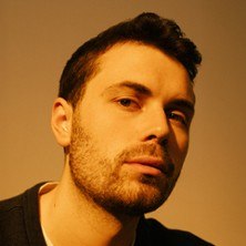 Ein Mann mit Bart und kurzem Haar blickt ernst in die Kamera. Der Hintergrund ist neutral gehalten., &copy; links im Bild