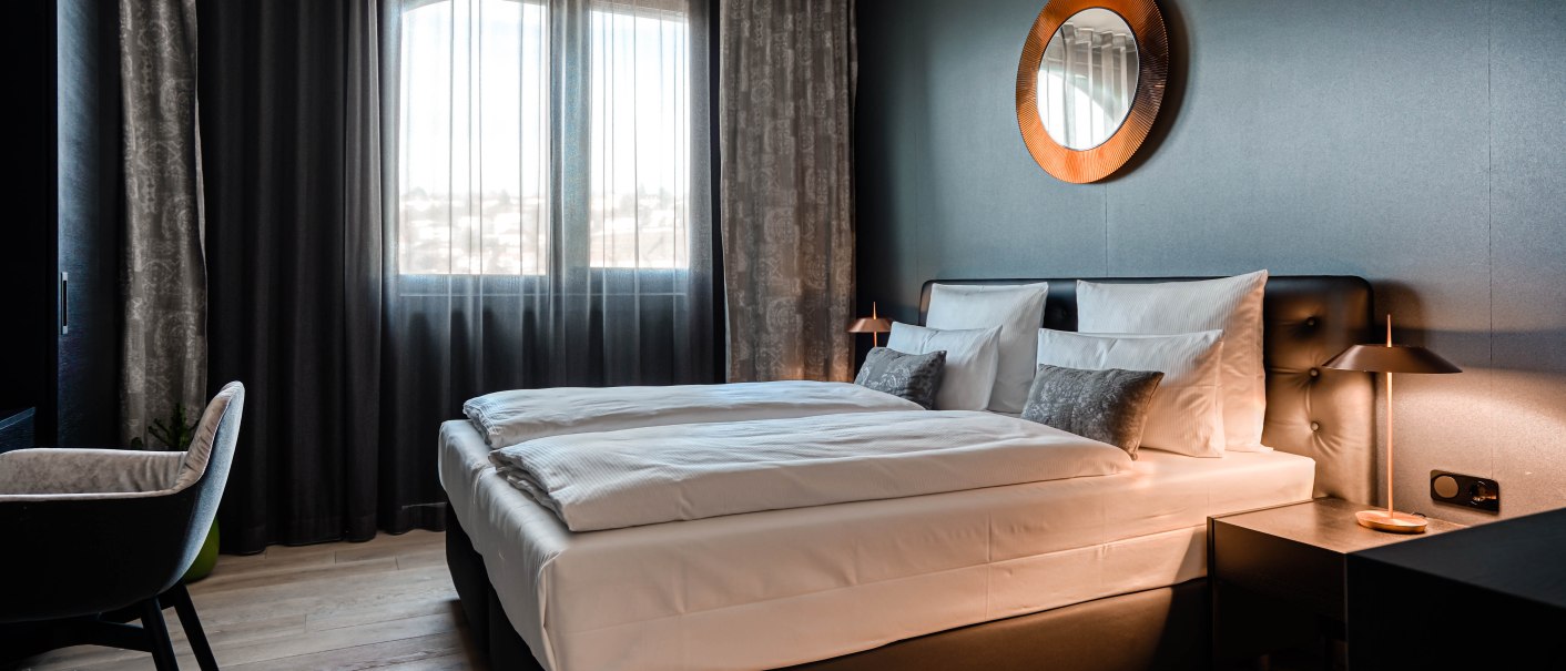 Modernes Schlafzimmer mit Doppelbett, dunklen Vorhängen und einem runden Spiegel an der Wand. Elegante Beleuchtung und Holzboden., © CLOUD N°7 APARTMENTS GmbH Modernes Schlafzimmer mit Doppelbett, dunklen Vorhängen und einem runden Spiegel an der Wand. Elegante Beleuchtung und Holzboden., © CLOUD N°7 APARTMENTS GmbH
