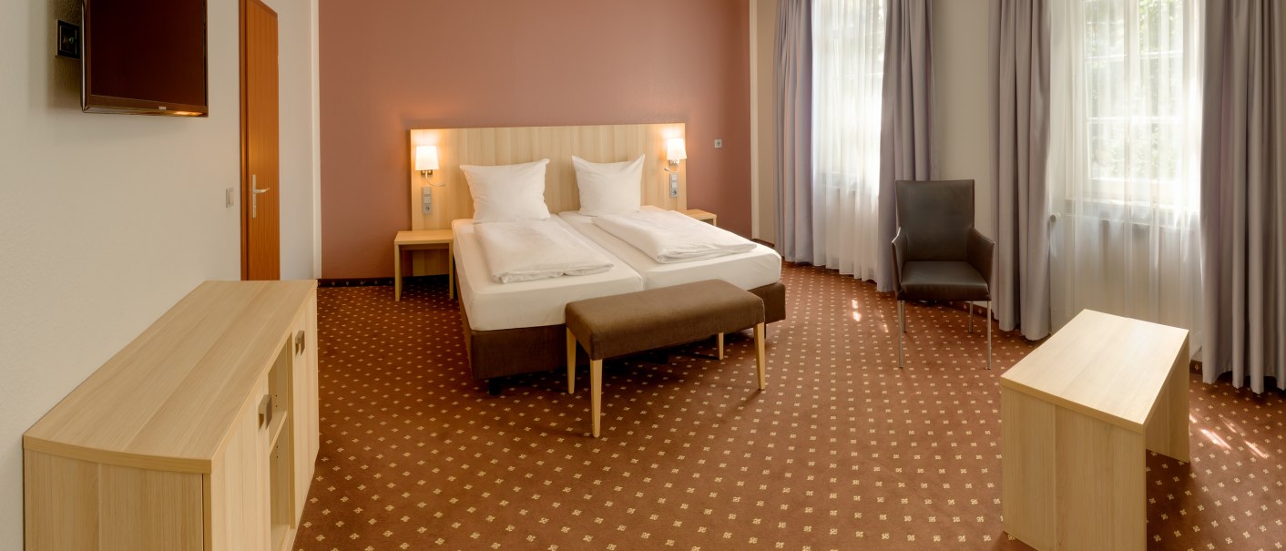 Spacious hotel room with double bed, brown carpet, TV, armchair and table. Large windows with curtains let in plenty of light., &copy; attimo Hotel Stuttgart