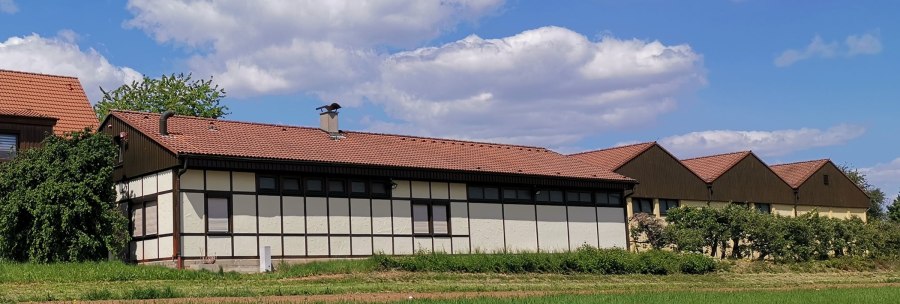 Half-timbered building with a red tiled roof, surrounded by green vegetation, under a blue sky with white clouds., © Weinbau Glock und Sohn GbR Half-timbered building with a red tiled roof, surrounded by green vegetation, under a blue sky with white clouds., © Weinbau Glock und Sohn GbR