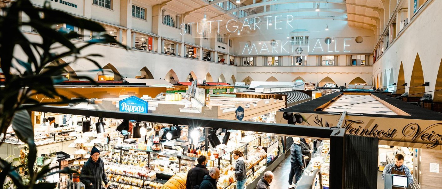 Blick von der Empore in die Stuttgarter Markthalle. Zahlreiche St&auml;nde und Besucher sind zu sehen, beleuchtet von hellem Licht., &copy; Stuttgart Marketing GmbH, Sarah Schmid