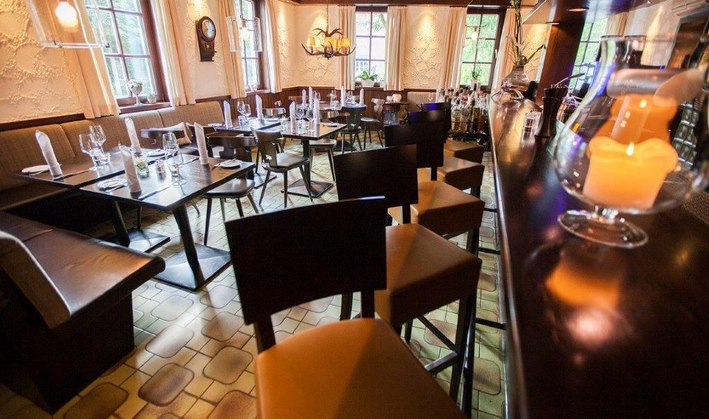 A cozy bar with set tables, candlelight, and a long counter. Wooden furniture and warm lighting create a welcoming atmosphere., &copy; Hotel Waldhorn