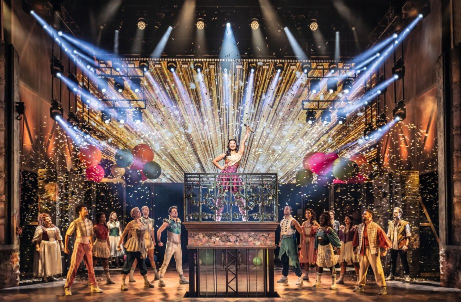 A dynamic stage scene from a musical with a woman in the center, surrounded by dancers, colorful lights and confetti., &copy; Johan Persson / Stage Entertainment