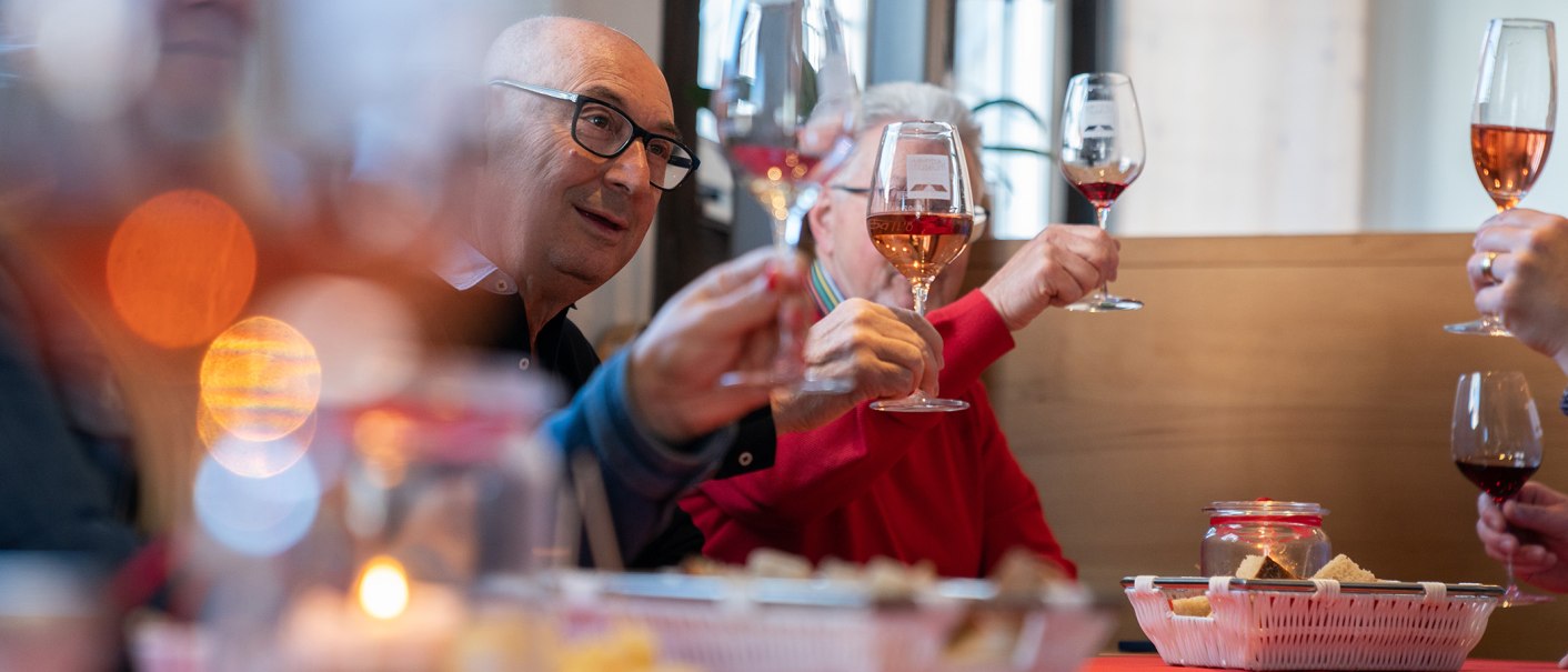 A group of people clink glasses of wine as they sit at a candlelit table with snacks., © Thomas Niedermüller A group of people clink glasses of wine as they sit at a candlelit table with snacks., © Thomas Niedermüller