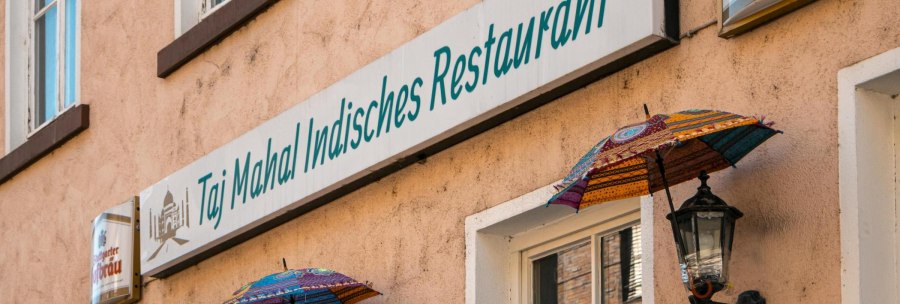 Fassade eines indischen Restaurants in Stuttgart mit bunten Schirmen und einem Schild mit der Aufschrift 'Taj Mahal Indisches Restaurant'., &copy; SMG, Sarah Schmid