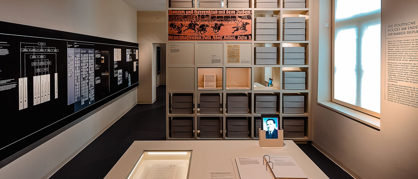 Ein Ausstellungsraum im HdG-Hotel Silber mit Dokumenten, Schautafeln und Archivboxen. Ein Bildschirm zeigt ein Porträt, daneben sind Texte und ein Fenster., © Daniel Stauch