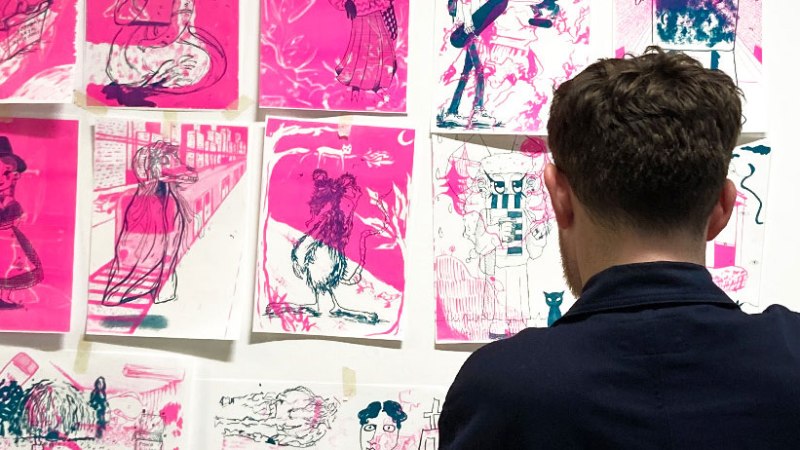 Ein Mann steht vor einer Wand mit pinkfarbenen Kunstwerken, die verschiedene Figuren und Szenen zeigen., &copy; StadtPalais