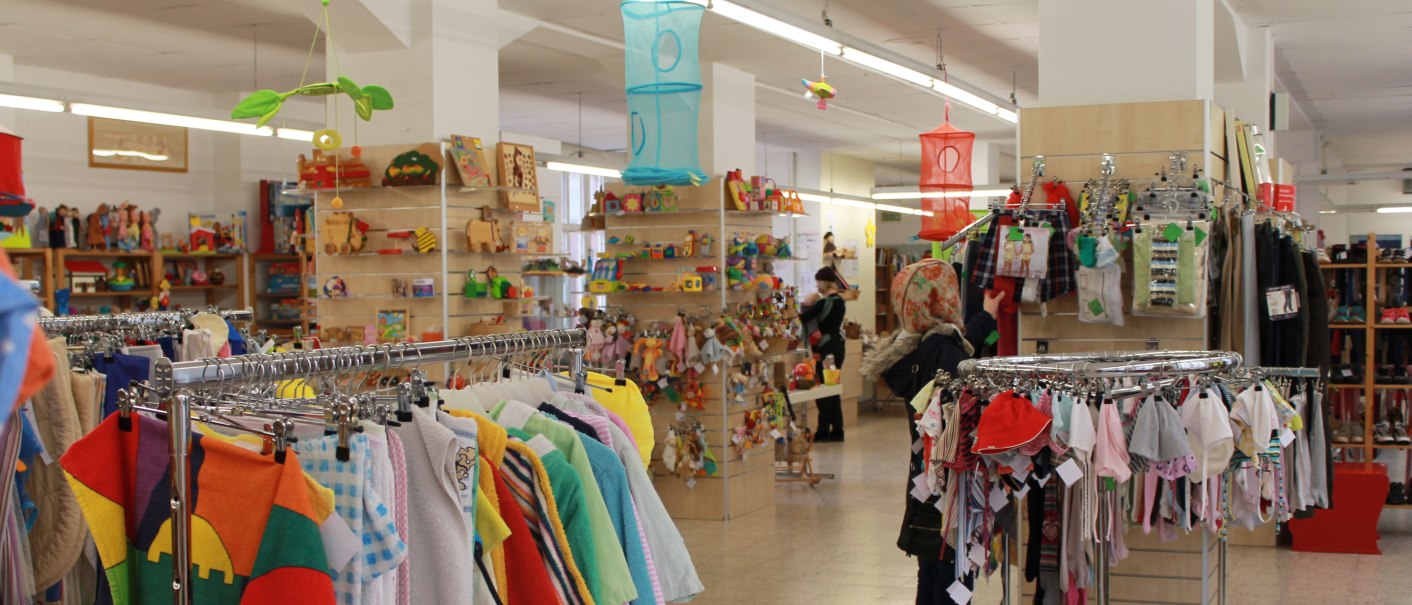 Ein Spielzeug- und Kinderbekleidungsgesch&auml;ft mit bunten Kleidungsst&uuml;cken und Spielzeugregalen. Eine Person betrachtet die ausgestellten Artikel., &copy; ZORA gGmbH