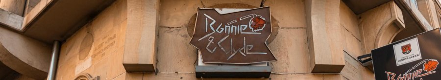 Ein Schild mit der Aufschrift 'Bonnie & Clyde' hängt an einem Gebäude. Die Fassade ist aus Stein, und es gibt dekorative Laternen., © SMG. Sarah Schmid Ein Schild mit der Aufschrift 'Bonnie & Clyde' hängt an einem Gebäude. Die Fassade ist aus Stein, und es gibt dekorative Laternen., © SMG. Sarah Schmid