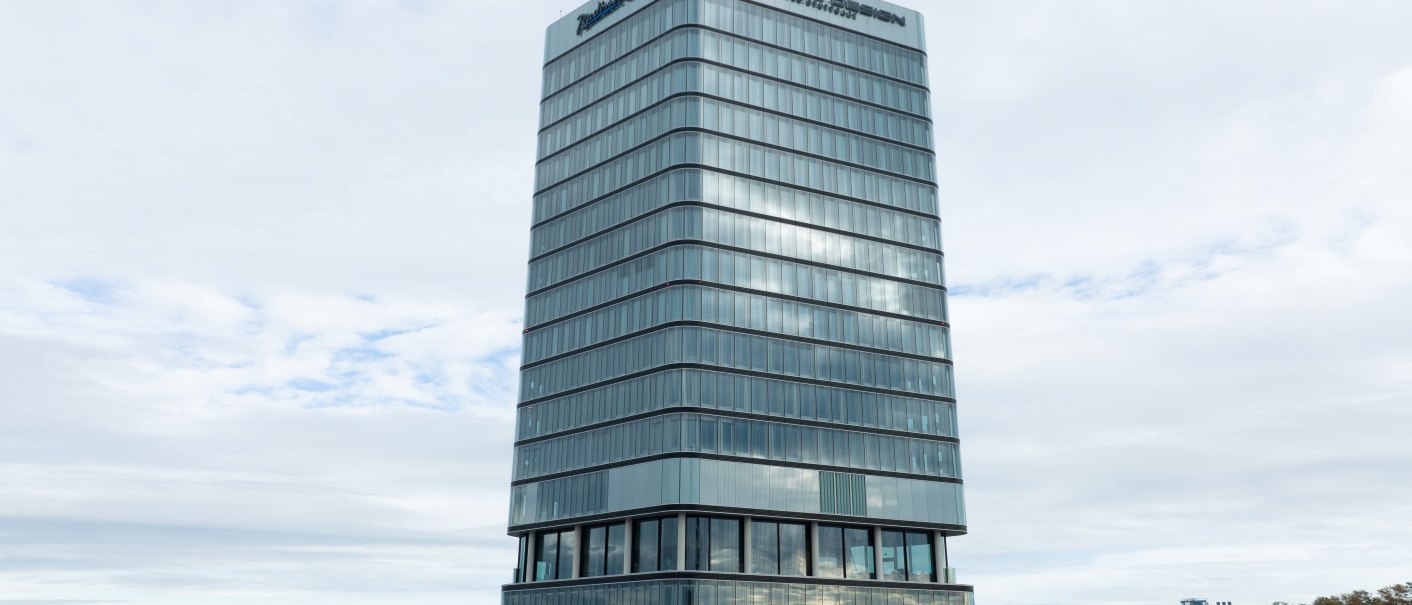 Ein modernes Hochhaus mit Glasfassade und dem Schriftzug 'Porsche Design' in einer st&auml;dtischen Umgebung., &copy; Radisson Hotel Group