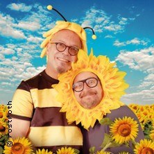 Zwei Personen in Bienen- und Sonnenblumenkostümen stehen lächelnd vor einem Sonnenblumenfeld unter blauem Himmel., © links im Bild Zwei Personen in Bienen- und Sonnenblumenkostümen stehen lächelnd vor einem Sonnenblumenfeld unter blauem Himmel., © links im Bild