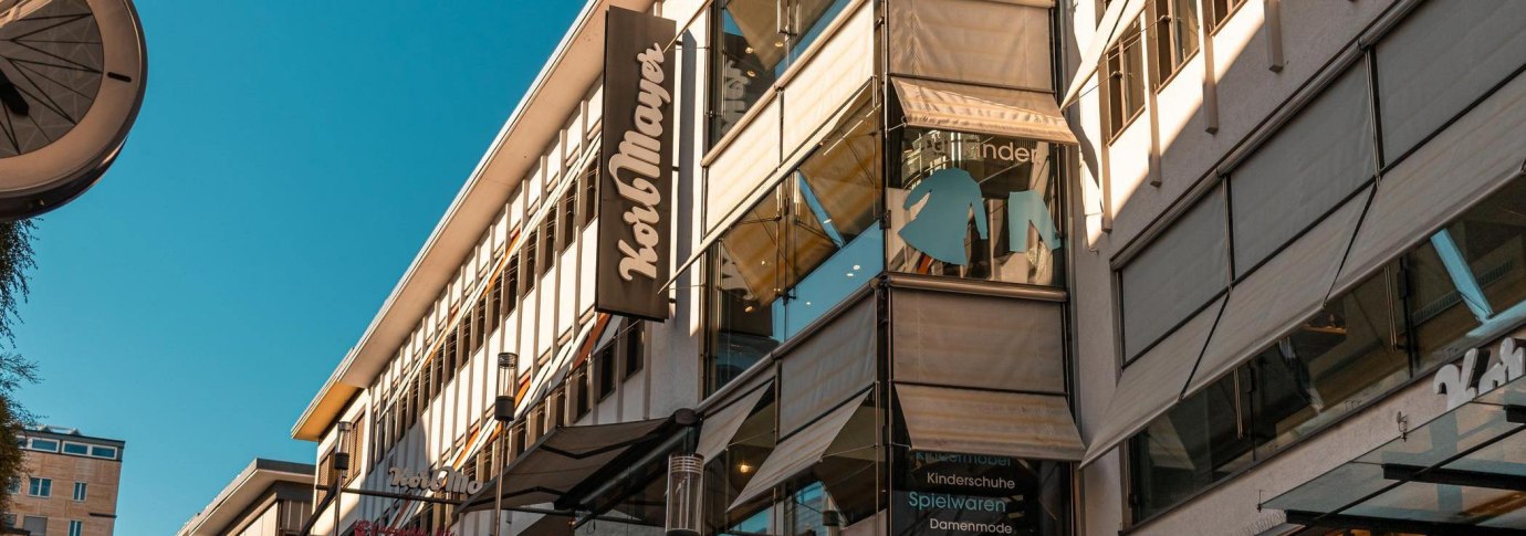 Gebäude mit Korbmayer-Schild, Schaufenster mit Kinderkleidung und Spielwaren. Moderne Architektur unter blauem Himmel., © Stuttgart Marketing GmbH, Sarah Schmid