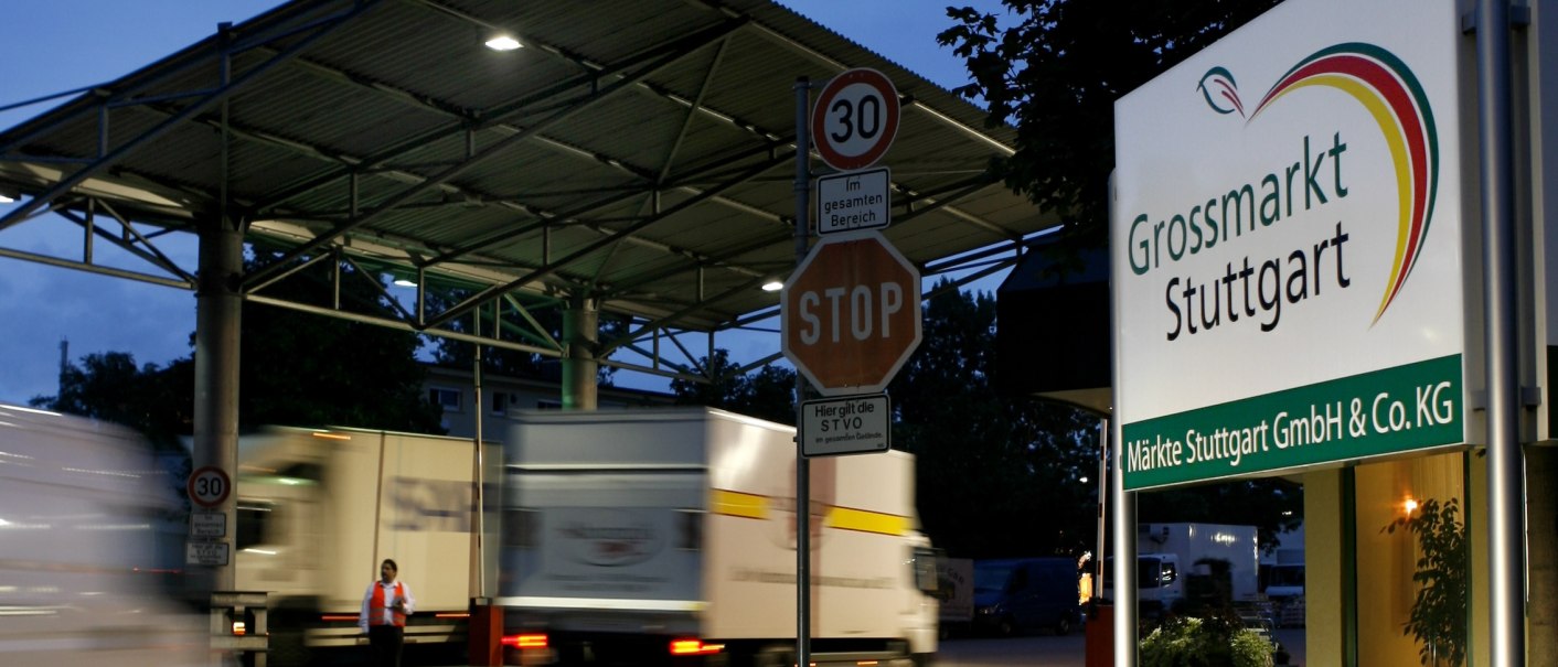 Einfahrt zum Gro&szlig;markt Stuttgart bei D&auml;mmerung. Lastwagen fahren vorbei, ein Stoppschild und ein Geschwindigkeitsbegrenzungsschild sind sichtbar., &copy; M&auml;rkte Stuttgart GmbH