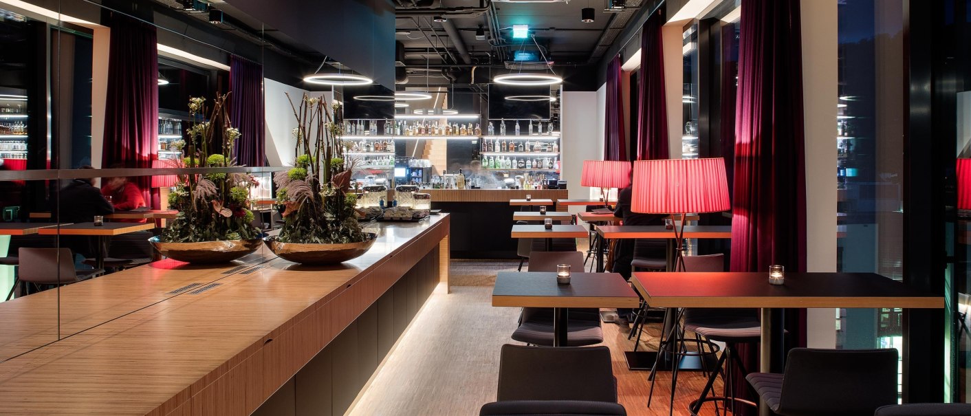 Modern bar on the 7th floor with stylish furnishings, red lamps and plant arrangements. Subdued lighting creates a cozy atmosphere., © Hotel am Remspark Modern bar on the 7th floor with stylish furnishings, red lamps and plant arrangements. Subdued lighting creates a cozy atmosphere., © Hotel am Remspark
