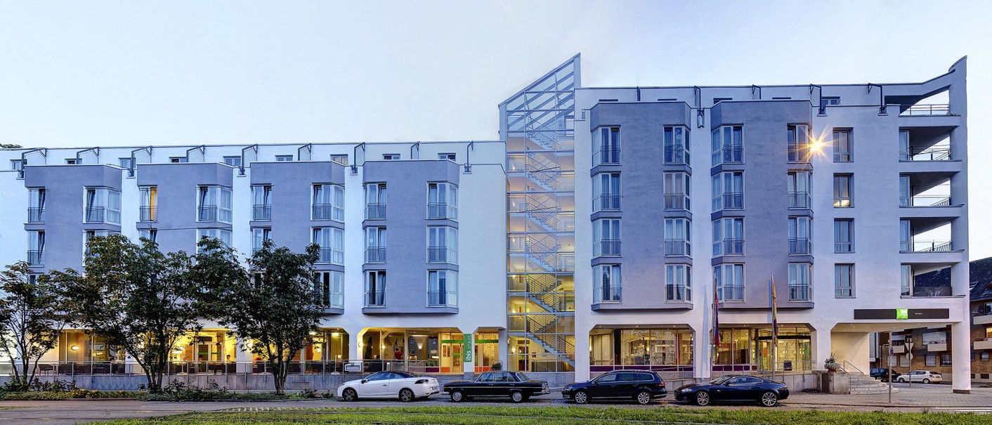 Modernes Hotelgebäude mit Glasfassade, beleuchteten Fenstern und parkenden Autos davor. Dämmerung sorgt für eine stimmungsvolle Beleuchtung., © Ibis Styles Stuttgart Modernes Hotelgebäude mit Glasfassade, beleuchteten Fenstern und parkenden Autos davor. Dämmerung sorgt für eine stimmungsvolle Beleuchtung., © Ibis Styles Stuttgart